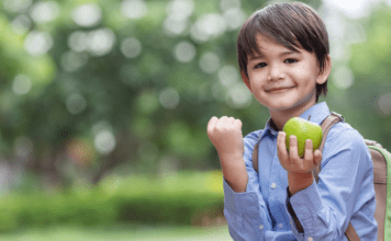 boy with backpack holds apple