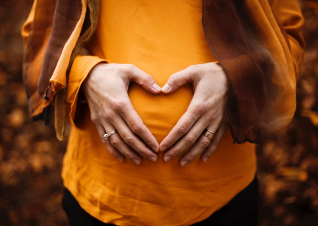 woman makes heart over pregnant belly