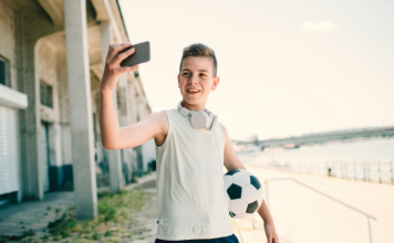 young boy holding soccer ball holds phone up, videoing himself