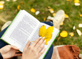 woman sits in grass reading using leaf as bookmark