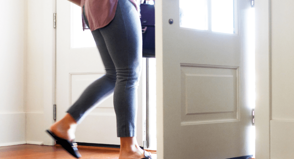 woman walks through open door carrying a bag
