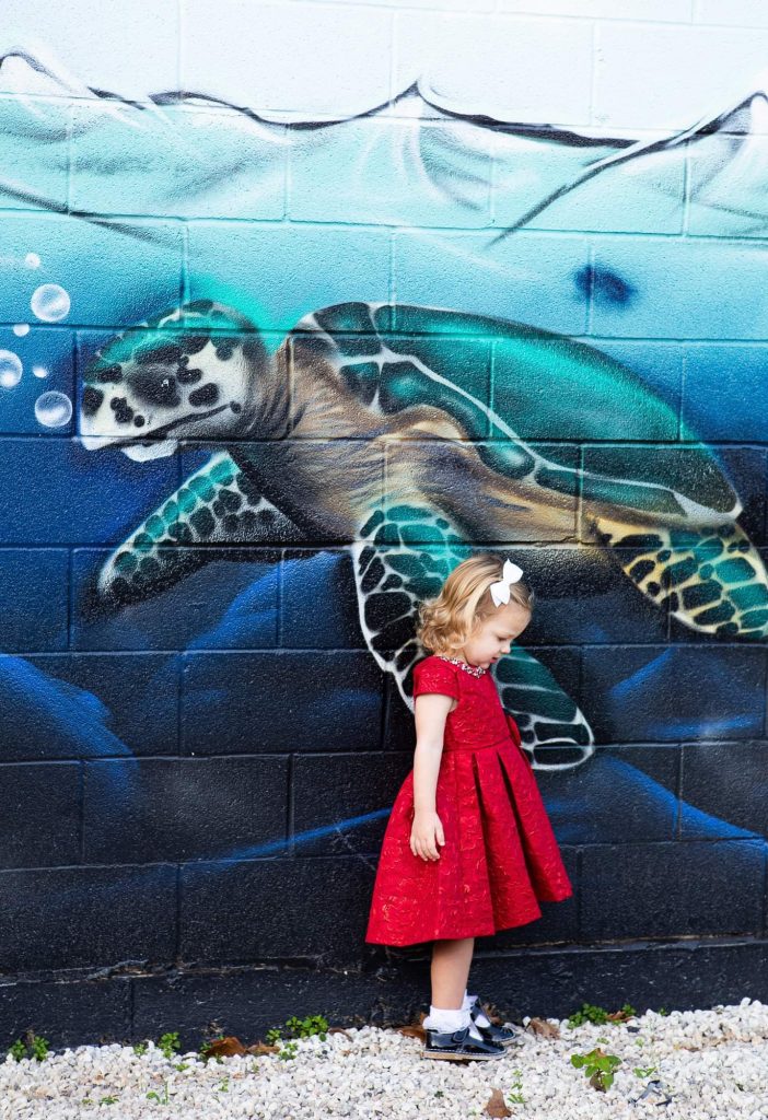 girl in red dress stands by mural of sea turtle