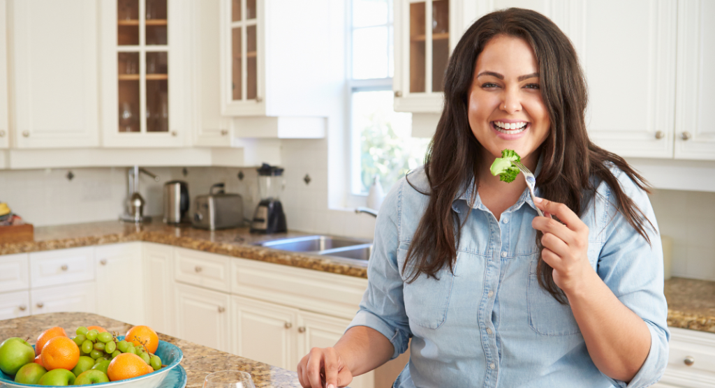 woman smiling while eating a bite of broccoli