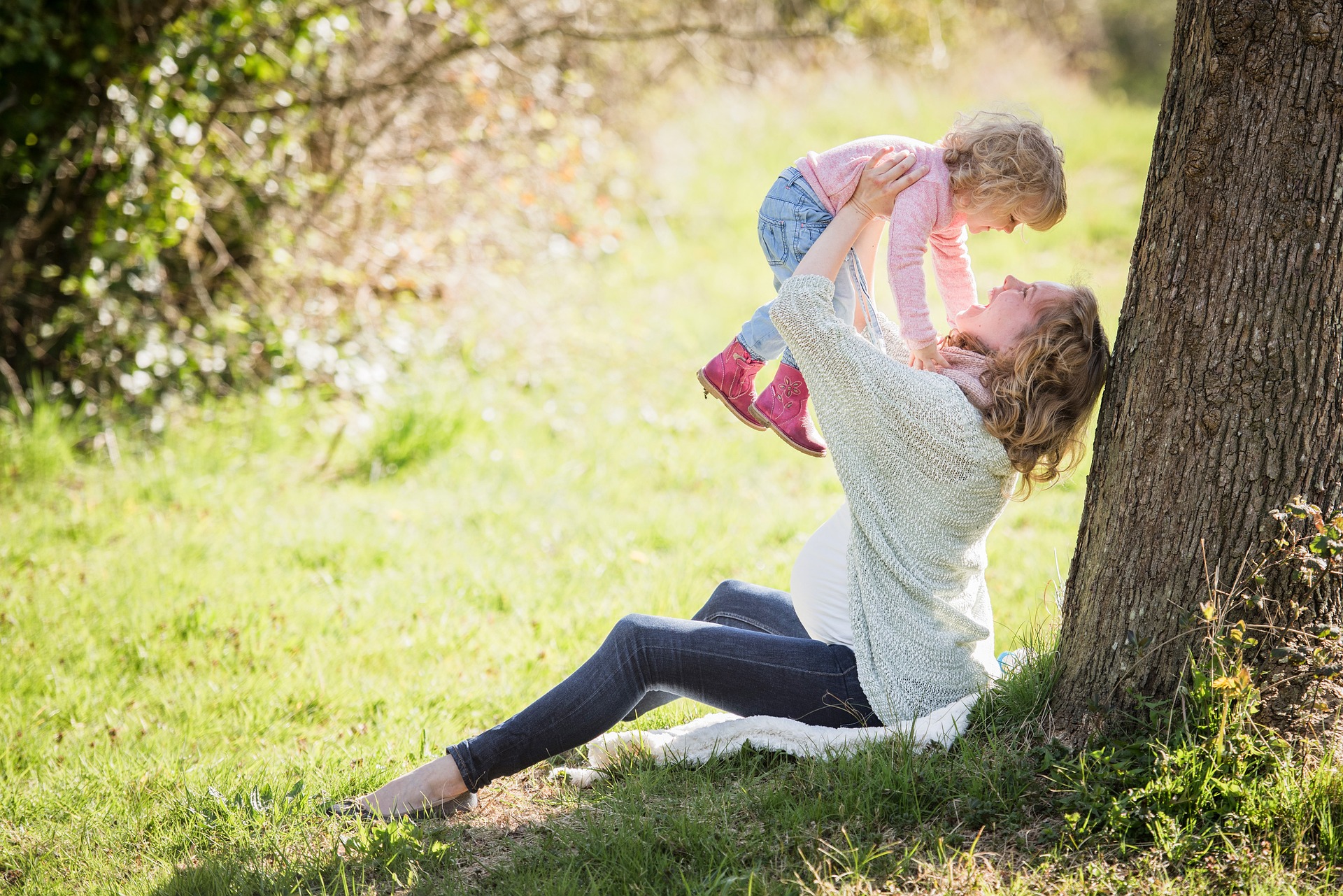 woman sits against tree and holds up toddler