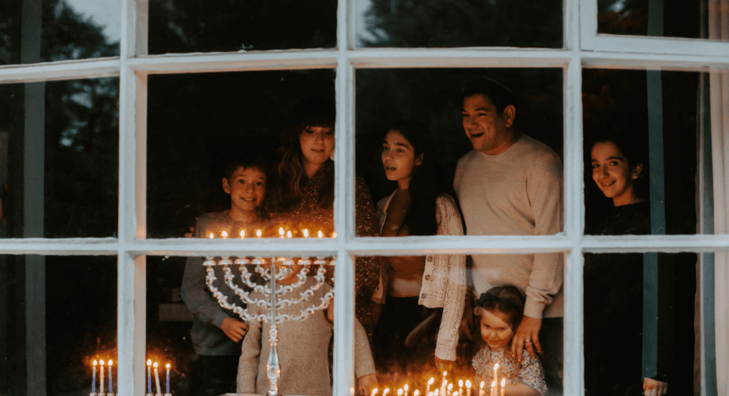 family stands in front of window looking at a Menorah