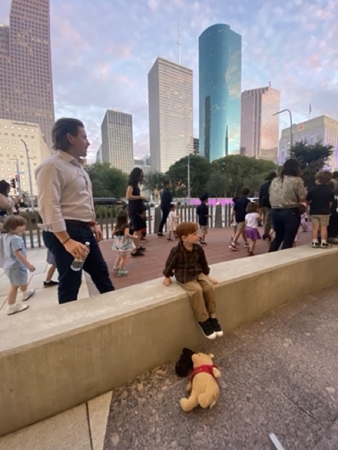 child sits on ledge with Houston skyline in background
