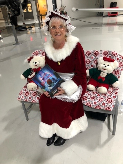 Mrs. Claus sits on bench holding a storybook