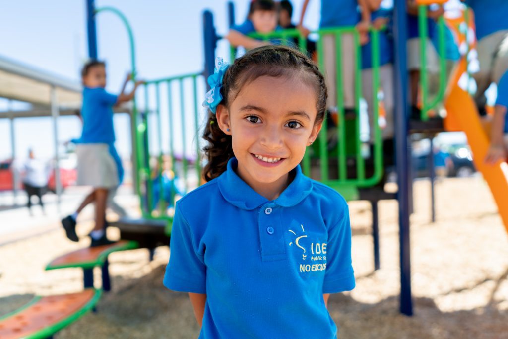 IDEA Public Schools student stands smiling on playground