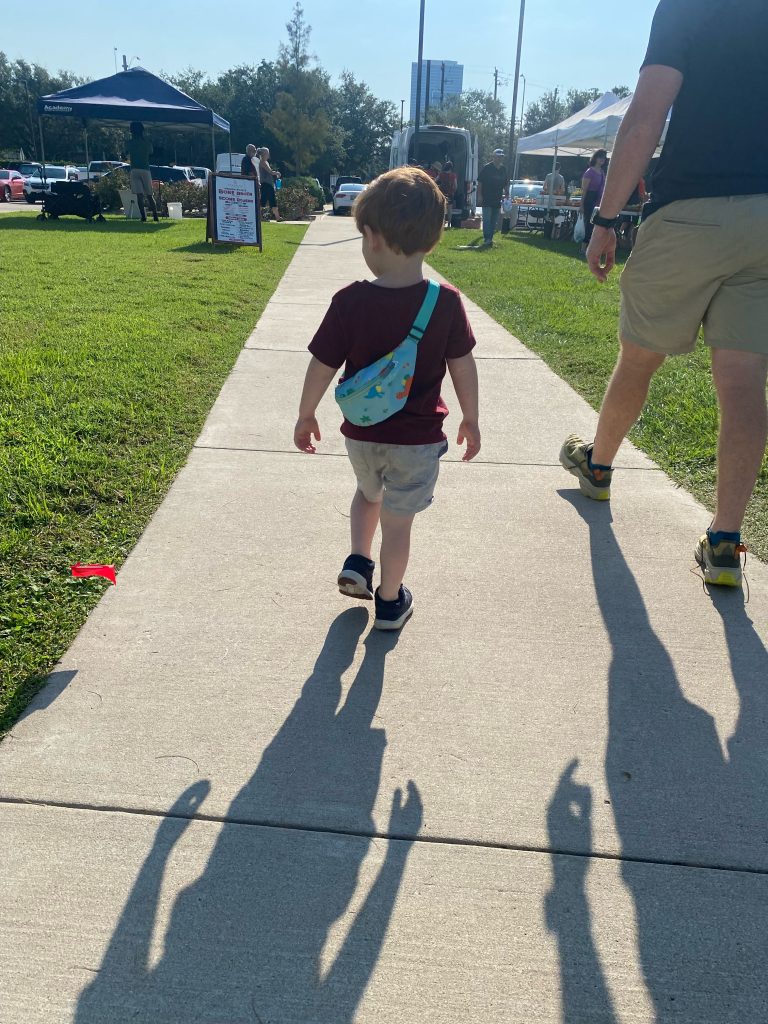 little boy with fanny pack walks on sidewalk