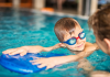 child with goggles looks at swim instructor while holding on to kickboard